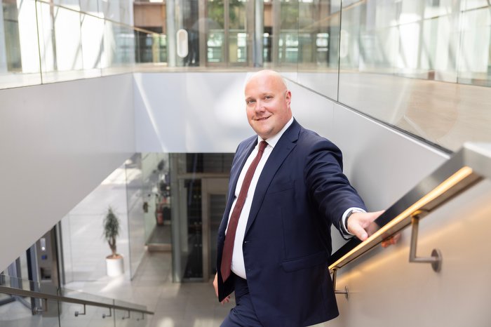 Man in pak loopt glimlachend een trap af in een modern kantoorgebouw met glazen wanden