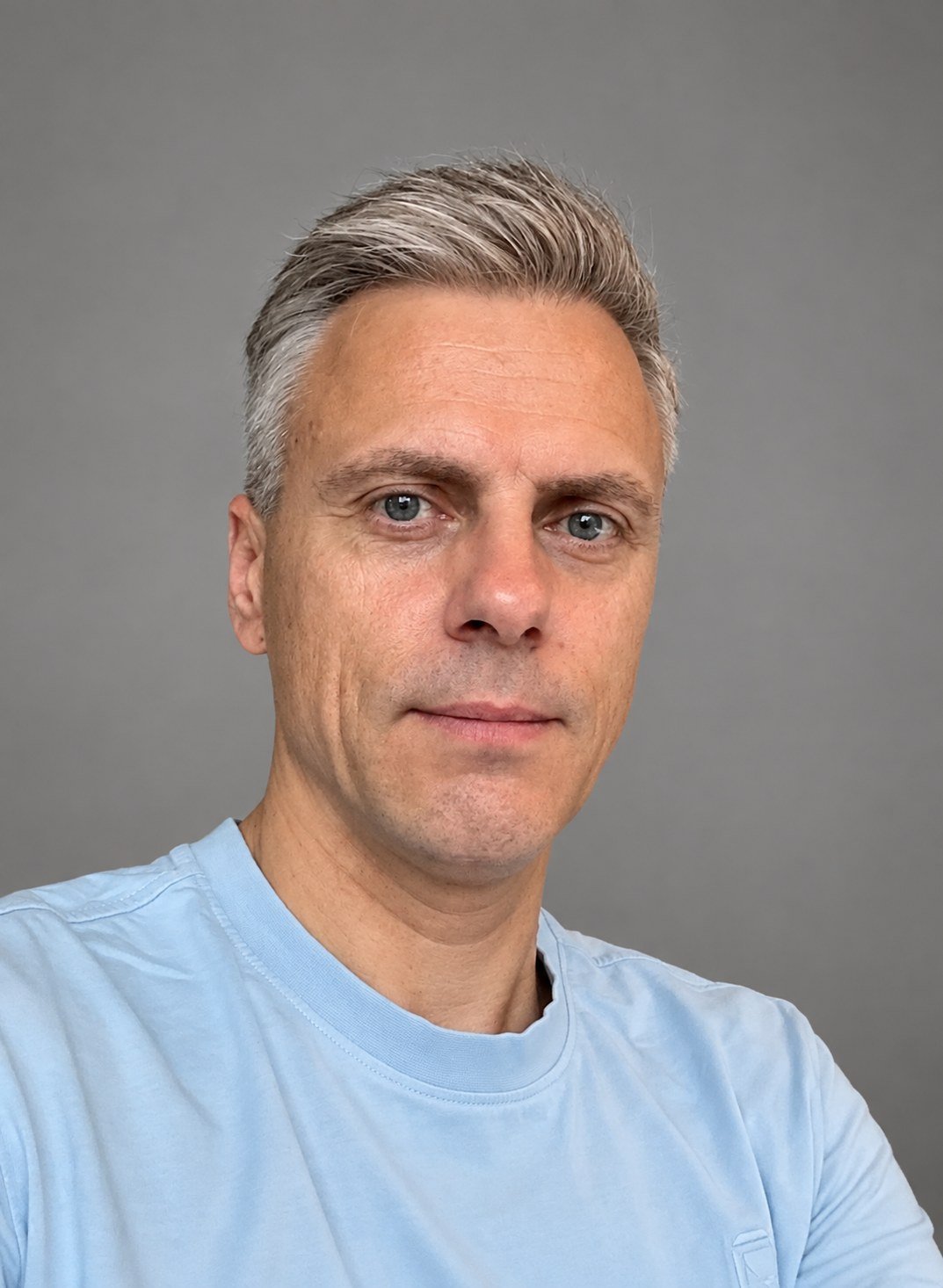 Portretfoto van een man met grijzend haar in lichtblauw shirt tegen een grijze achtergrond